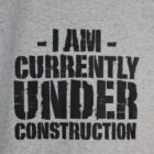 A t-shirt featuring the phrase "I am currently under construction" in bold, playful lettering, conveying a sense of humor.